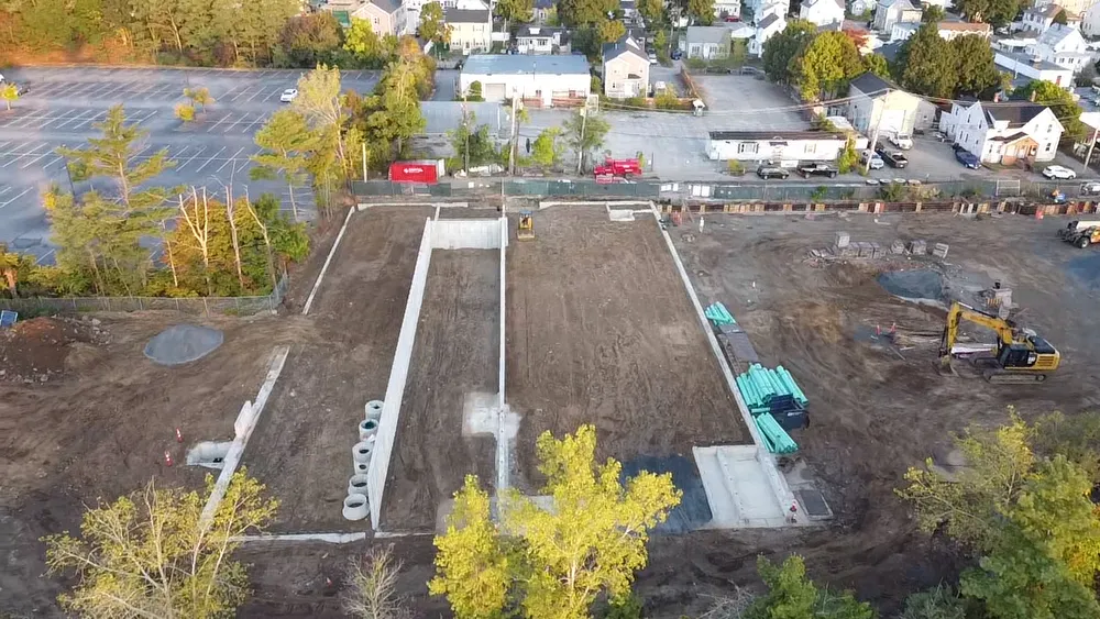 Wide-angle aerial shot of Avalon Quincy construction site with precast foundation walls and pipes being laid